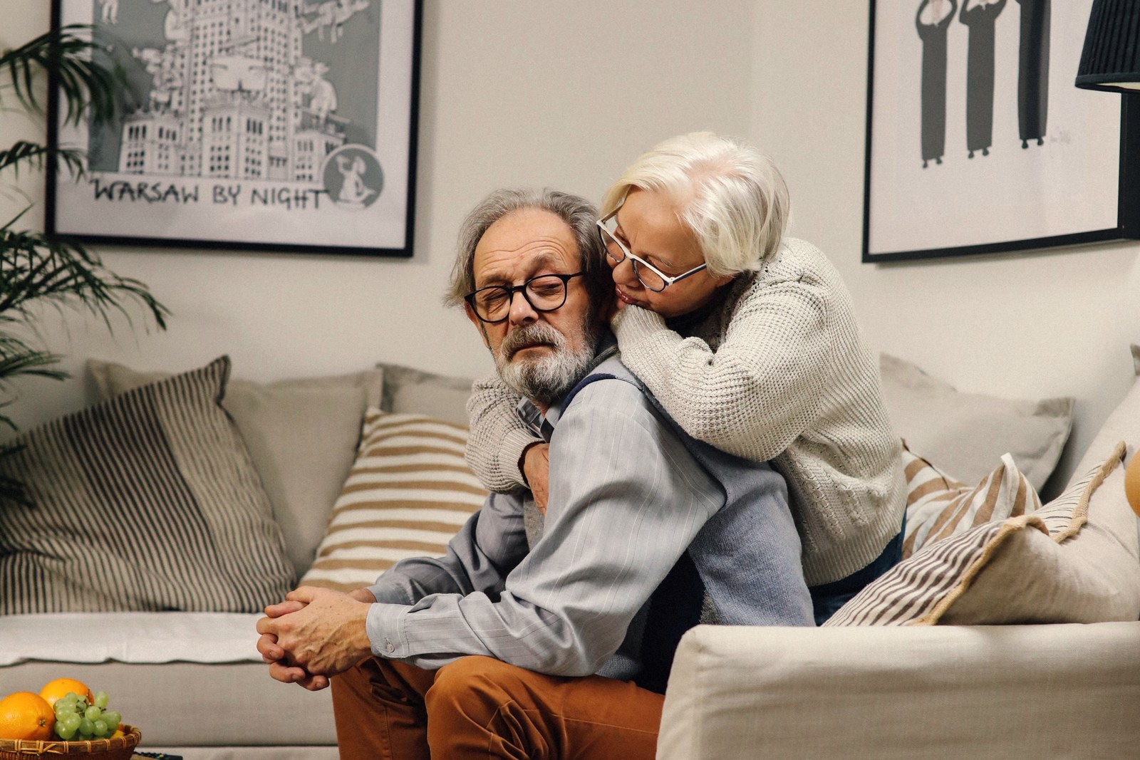 Casal de idosos sentado no sofá de casa, se consolando, ilustrando o risco do fiador perder o imóvel da família