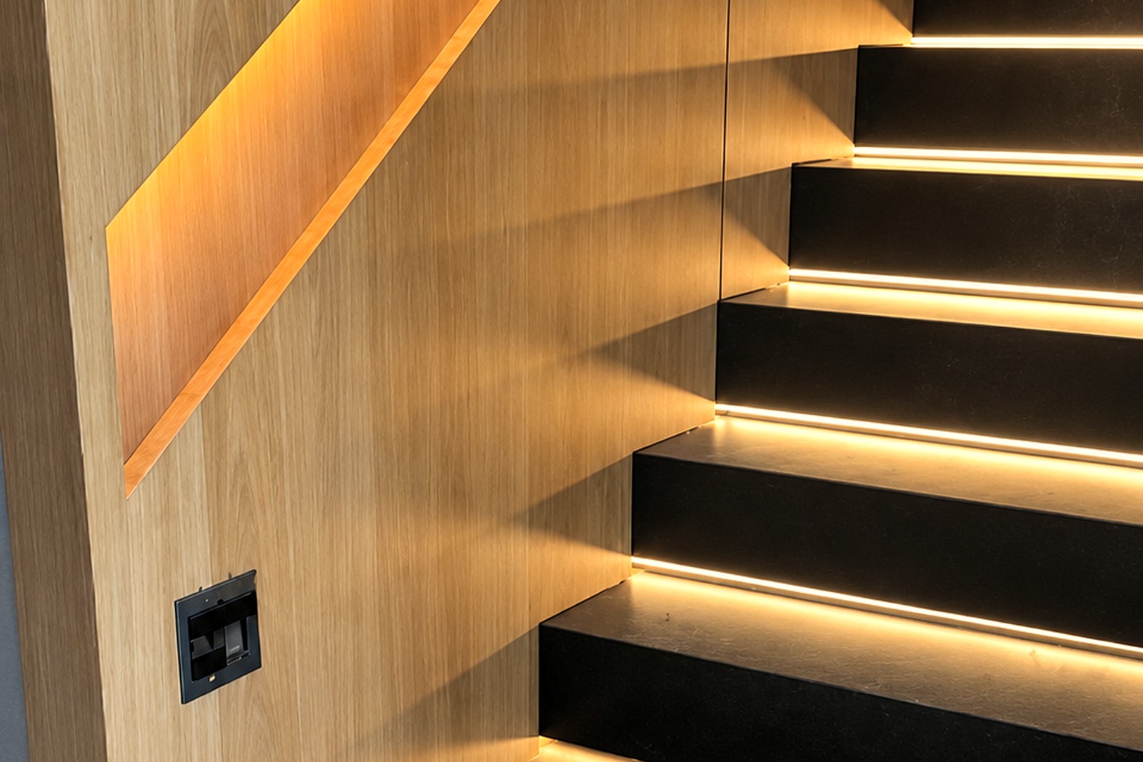 Escada com painel de madeira, corrimão embutido iluminado e degraus pretos com LED